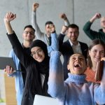A diverse team of business professionals ecstatically celebrating their success in a modern office, expressing triumph and unity after achieving their goals.